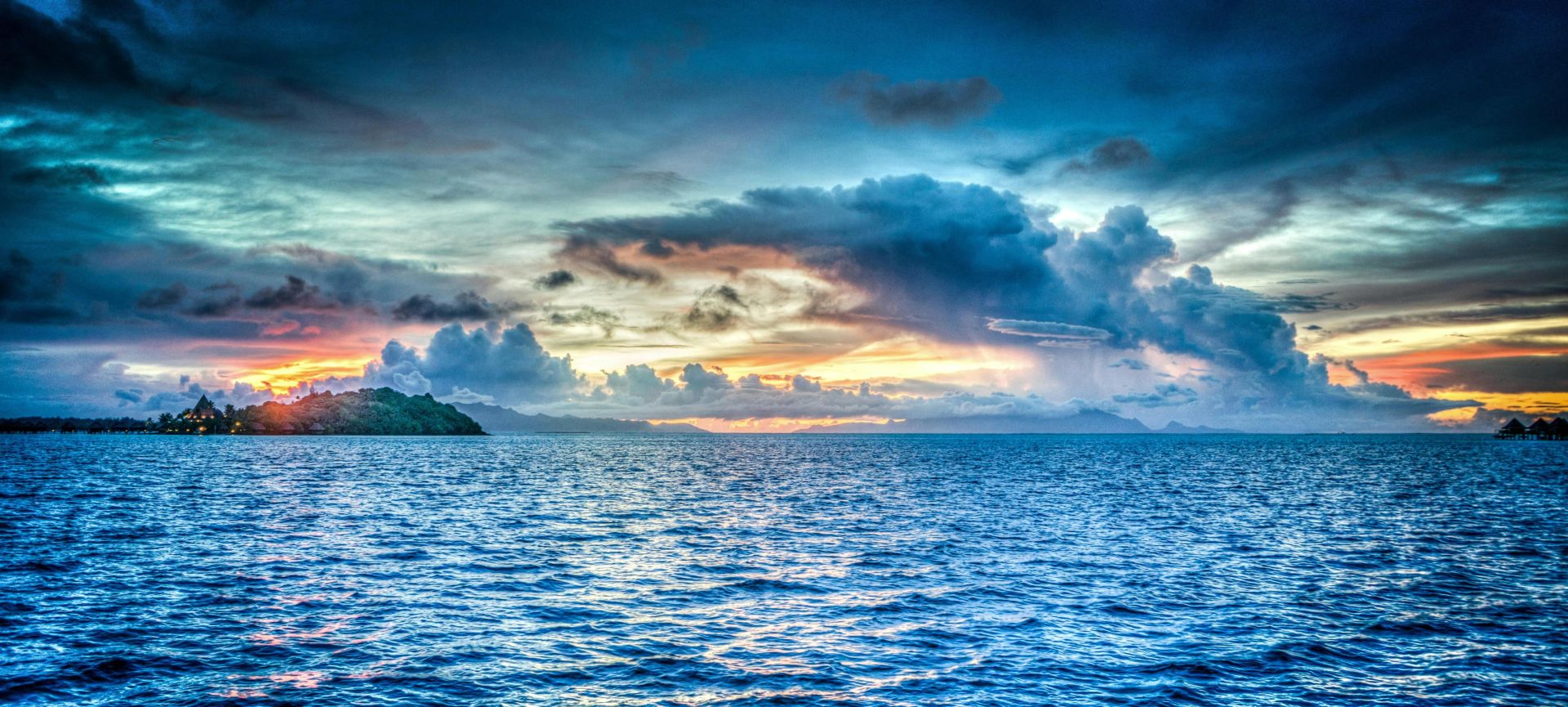 Vibrant sunset over tropical ocean with dramatic clouds and distant island.