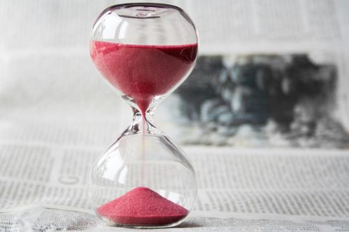 Close-up of a transparent hourglass with pink sand flowing, placed on a newspaper background.