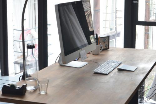 A sleek, minimalist office setup featuring a computer on a wooden desk with natural daylight.