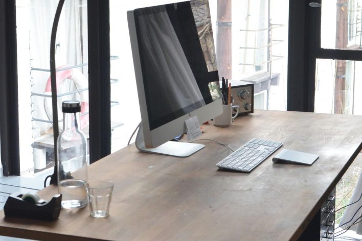 A sleek, minimalist office setup featuring a computer on a wooden desk with natural daylight.