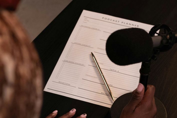 An overhead view of a person with a microphone and podcast planner on a desk.
